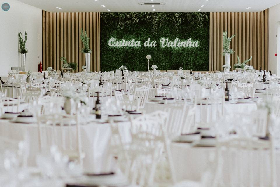 Salão de banquetes com mesas brancas e parede verde